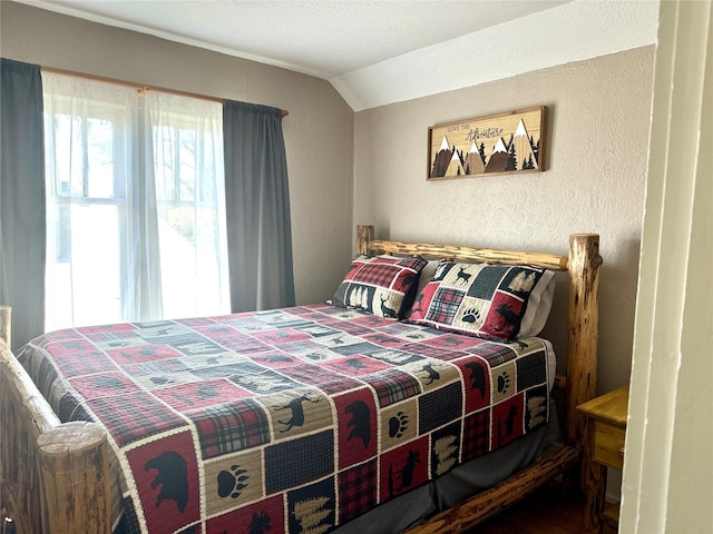bedroom featuring lofted ceiling, a textured wall, and wood finished floors