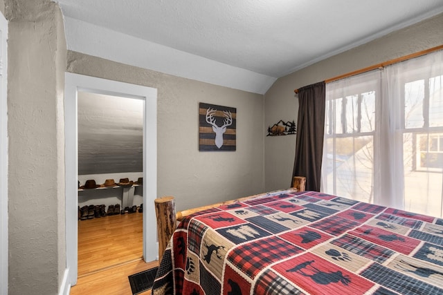 bedroom with lofted ceiling, a textured wall, and wood finished floors