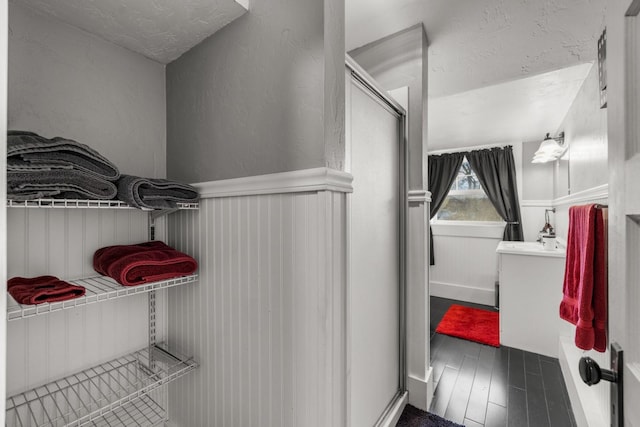 bathroom featuring vanity, a shower with door, wood finished floors, and a wainscoted wall