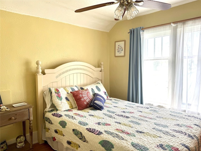 bedroom with vaulted ceiling, a textured wall, wood finished floors, and ceiling fan