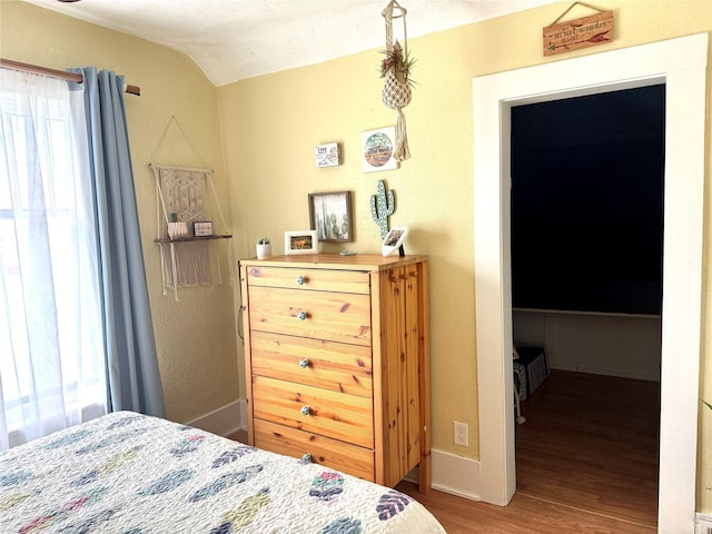 bedroom featuring lofted ceiling, a textured wall, and wood finished floors