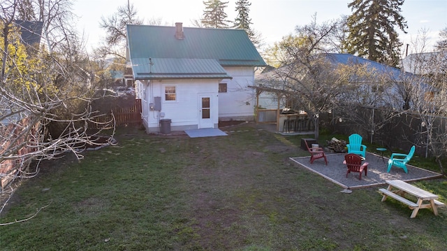 rear view of property with a lawn, a fenced backyard, a fire pit, and metal roof