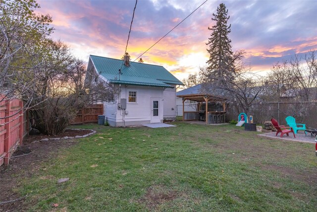 back of property at dusk featuring a gazebo, a patio area, a lawn, a fenced backyard, and metal roof