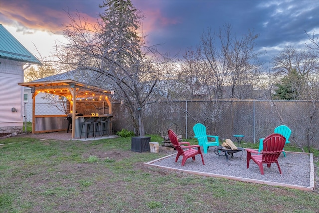 yard at dusk with a fire pit, outdoor dry bar, and fence