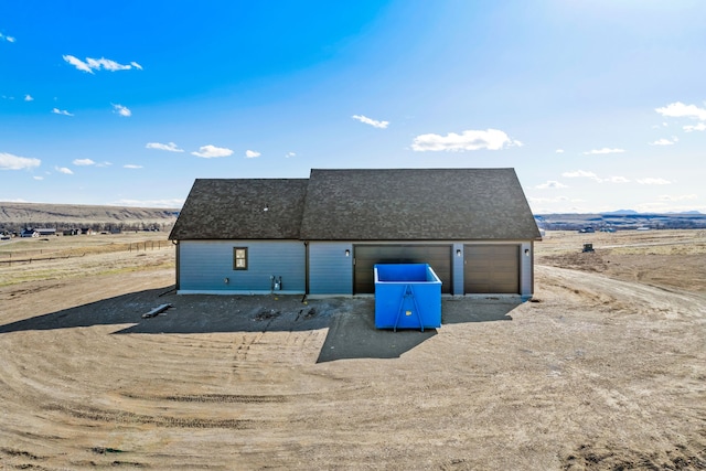 rear view of property with dirt driveway, an outbuilding, roof with shingles, and a garage
