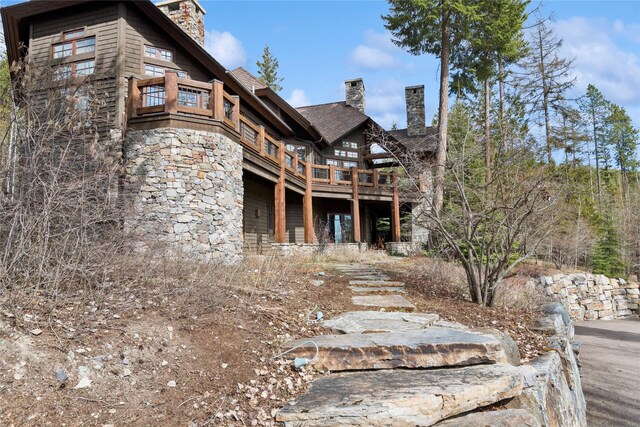 231 Arrowhead Dr, Whitefish, MT 59937 - back of house featuring a chimney, stone siding, a balcony, and roof with shingles