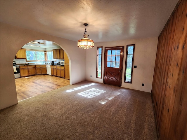 unfurnished dining area featuring arched walkways, a chandelier, and light carpet