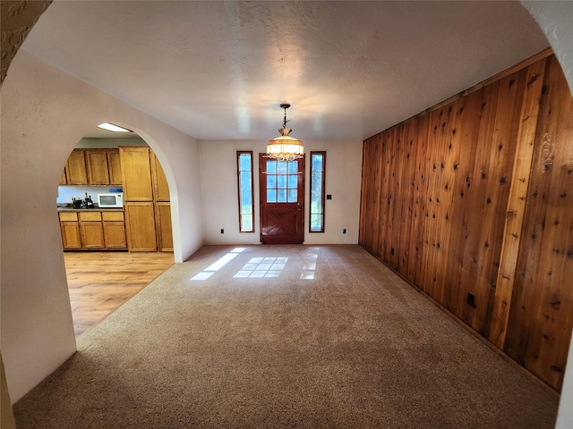 foyer featuring arched walkways, a notable chandelier, wood walls, and light carpet