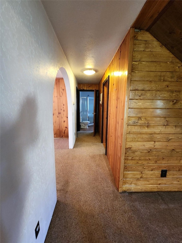corridor featuring arched walkways, wooden walls, and carpet floors