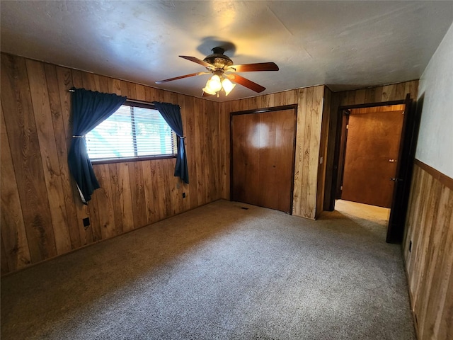 unfurnished bedroom with wooden walls, carpet, a closet, and a ceiling fan