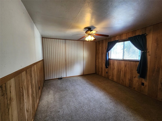 carpeted empty room with wood walls and a ceiling fan