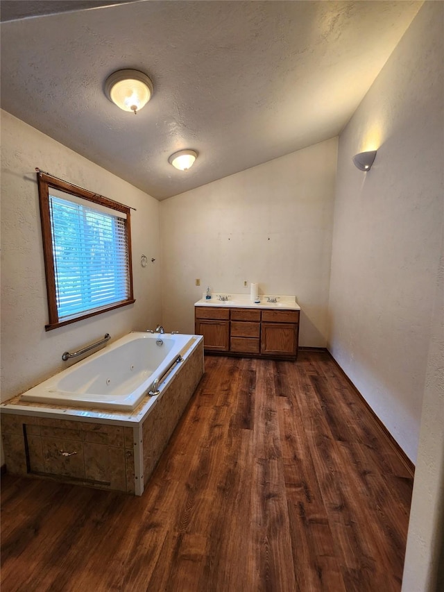 full bath with wood finished floors, a textured ceiling, a sink, and a tub with jets