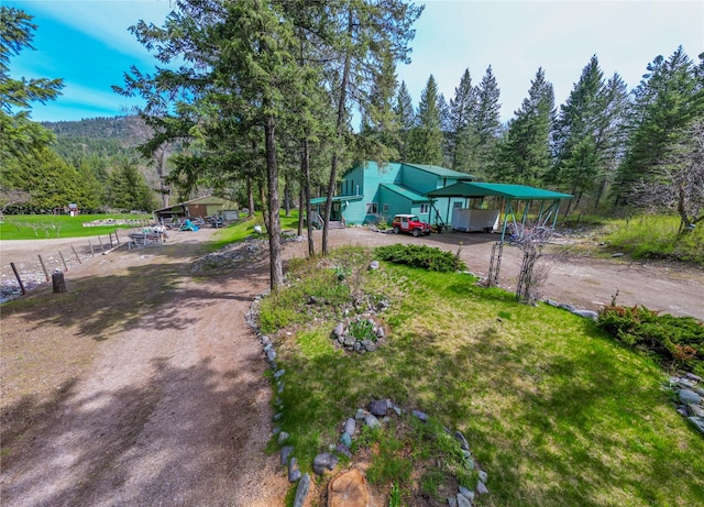 exterior space featuring a view of trees, a carport, and dirt driveway