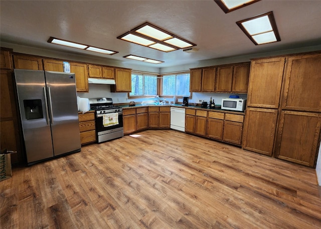 kitchen featuring stainless steel appliances, a sink, light wood-type flooring, brown cabinetry, and under cabinet range hood