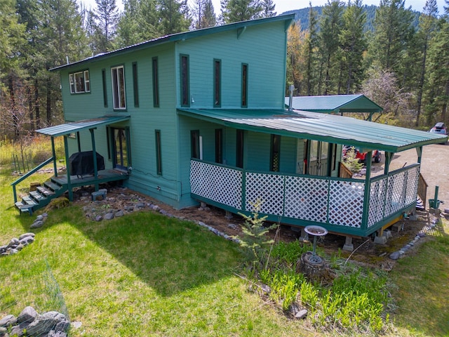back of house with covered porch, a yard, and metal roof