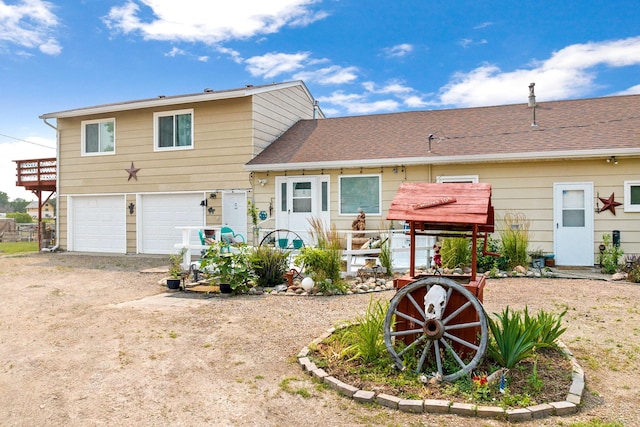 back of property with dirt driveway, roof with shingles, and a garage