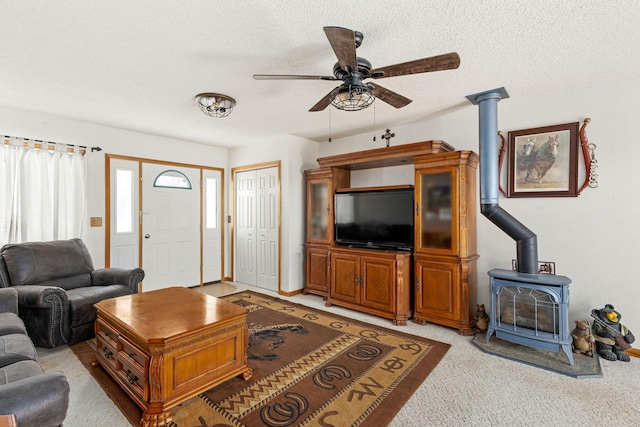 living room featuring light colored carpet, a ceiling fan, a wood stove, and a textured ceiling
