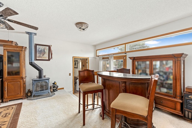 interior space with ceiling fan, light carpet, a textured ceiling, and a wood stove