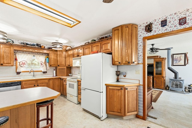 kitchen featuring a ceiling fan, white appliances, a wood stove, light countertops, and a breakfast bar area