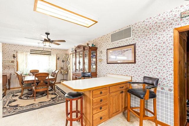 kitchen with wallpapered walls, a breakfast bar area, ceiling fan, light countertops, and a peninsula