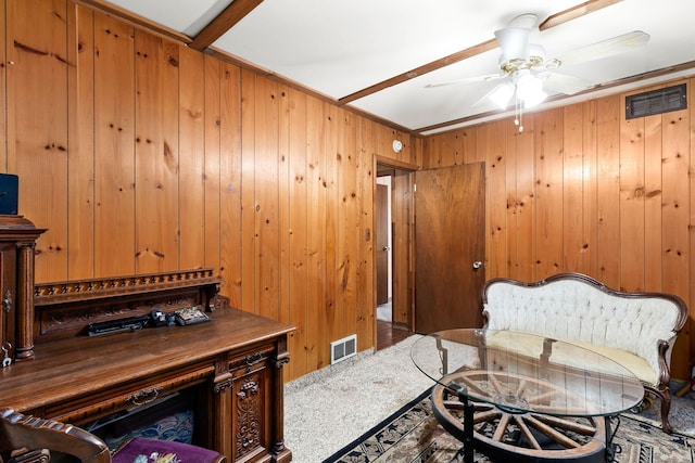 sitting room with a ceiling fan, visible vents, and wooden walls
