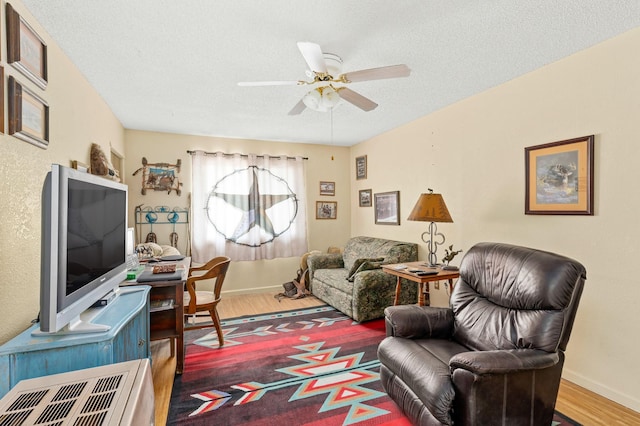 living area with baseboards, a ceiling fan, wood finished floors, and a textured ceiling