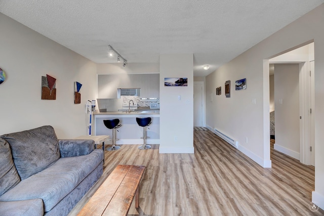 living room with a baseboard heating unit, baseboards, a textured ceiling, and light wood finished floors
