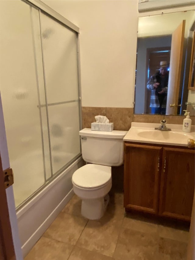 full bath with tile patterned floors, wainscoting, vanity, bath / shower combo with glass door, and toilet