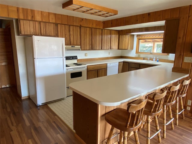 kitchen featuring a sink, brown cabinets, white appliances, a peninsula, and under cabinet range hood