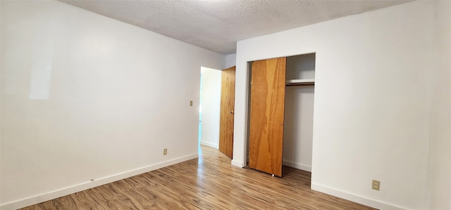 unfurnished bedroom with baseboards, light wood-style floors, a textured ceiling, and a closet