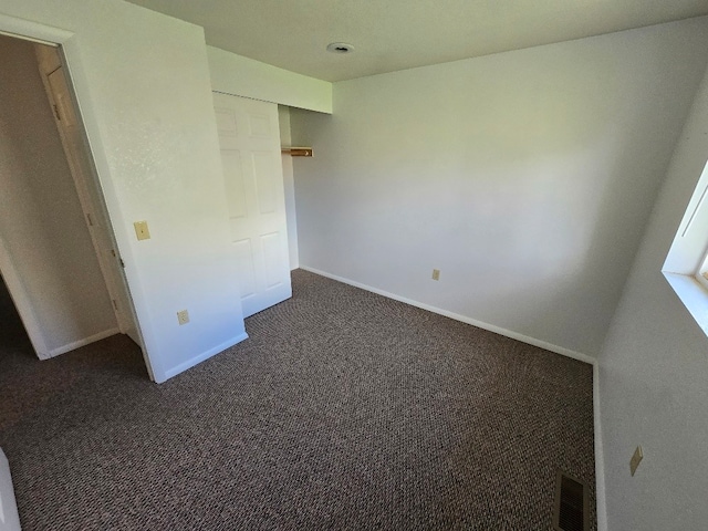 unfurnished bedroom featuring baseboards, dark colored carpet, and visible vents
