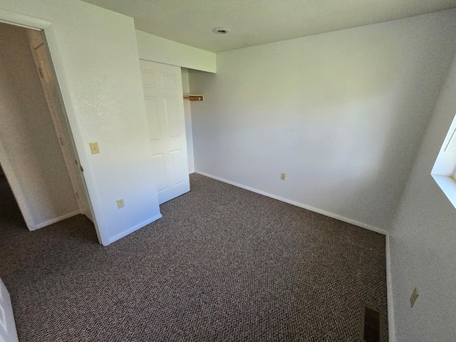 unfurnished bedroom with dark carpet, visible vents, and baseboards