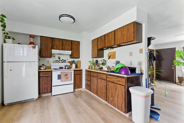 kitchen featuring light wood-type flooring, white appliances, brown cabinetry, light countertops, and under cabinet range hood