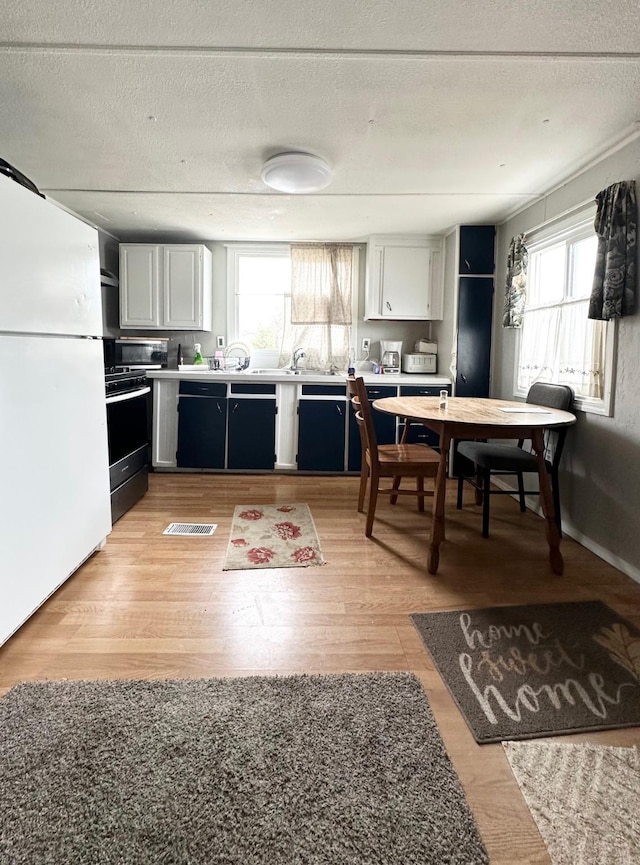 kitchen with stove, light wood-style flooring, stainless steel microwave, black dishwasher, and freestanding refrigerator