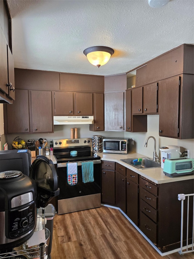 kitchen featuring stainless steel appliances, a sink, dark wood finished floors, light countertops, and under cabinet range hood