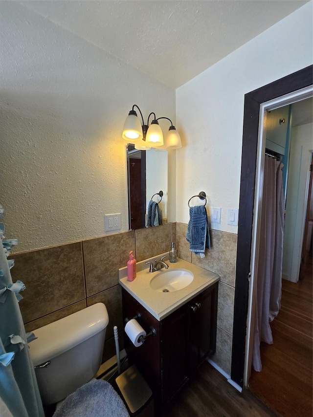 bathroom with wood finished floors, vanity, tile walls, a wainscoted wall, and toilet