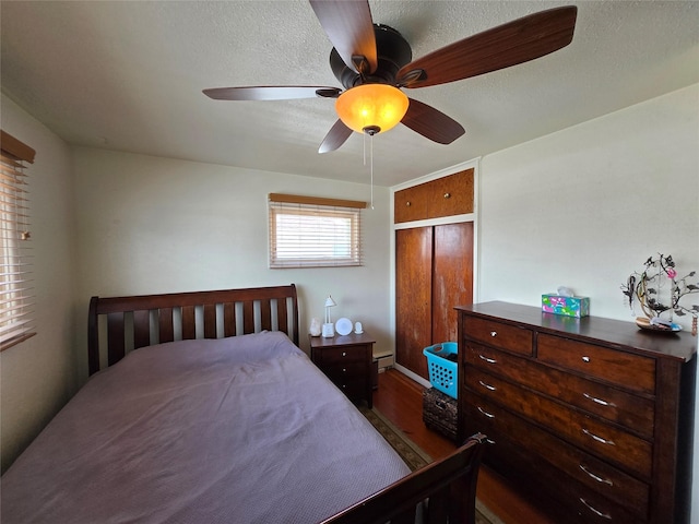 bedroom with a baseboard heating unit, a closet, dark wood-style floors, and ceiling fan