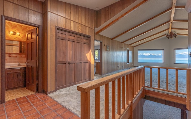 hall with tile patterned floors, a sink, lofted ceiling with beams, a water view, and wood walls