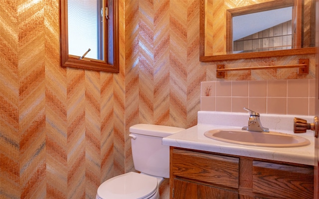 bathroom with vaulted ceiling, decorative backsplash, vanity, tile walls, and toilet