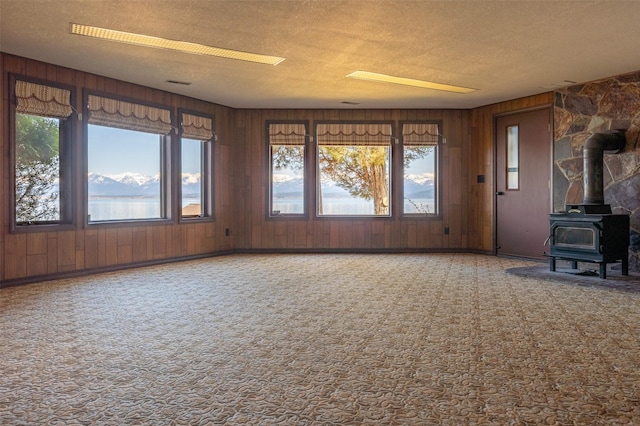 unfurnished living room featuring wood walls, a wood stove, visible vents, carpet floors, and a textured ceiling