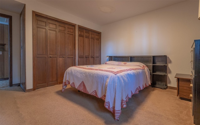 bedroom featuring light colored carpet, baseboards, and two closets