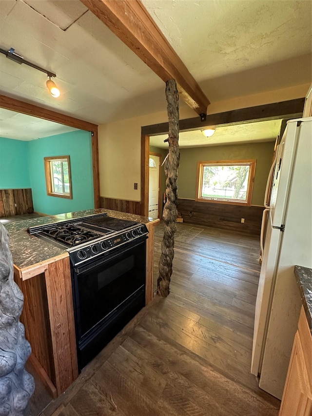 kitchen featuring a wainscoted wall, dark wood finished floors, freestanding refrigerator, black gas range, and beamed ceiling