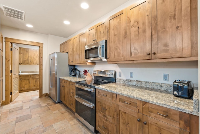 105 Oliver Ln Unit 7, Bigfork, MT 59911 - kitchen with appliances with stainless steel finishes, recessed lighting, stone finish floors, light stone counters, and brown cabinetry