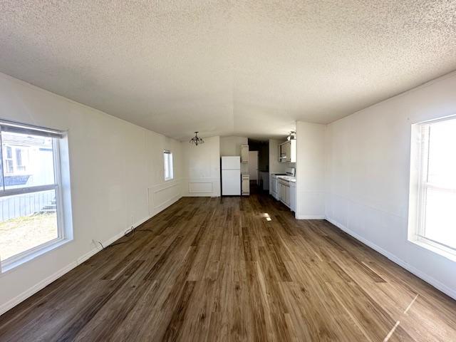unfurnished living room featuring dark wood finished floors, lofted ceiling, a chandelier, and a textured ceiling