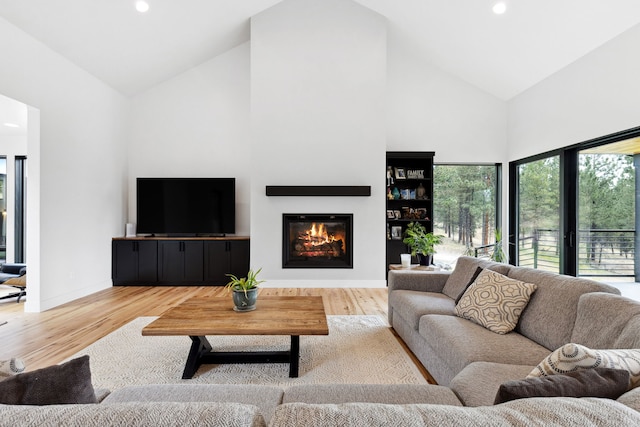 living area with wood finished floors, a glass covered fireplace, high vaulted ceiling, and recessed lighting