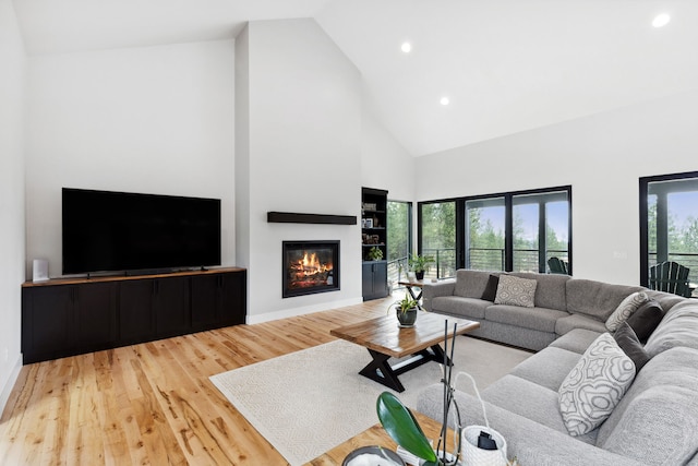 living room with high vaulted ceiling, a glass covered fireplace, wood finished floors, and recessed lighting