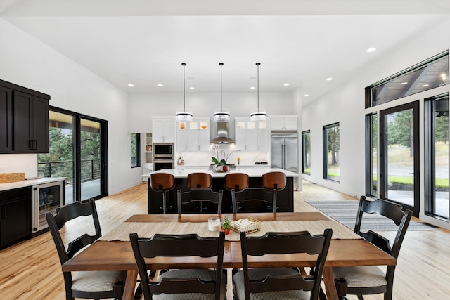 dining room with wine cooler, baseboards, a towering ceiling, recessed lighting, and light wood-style floors