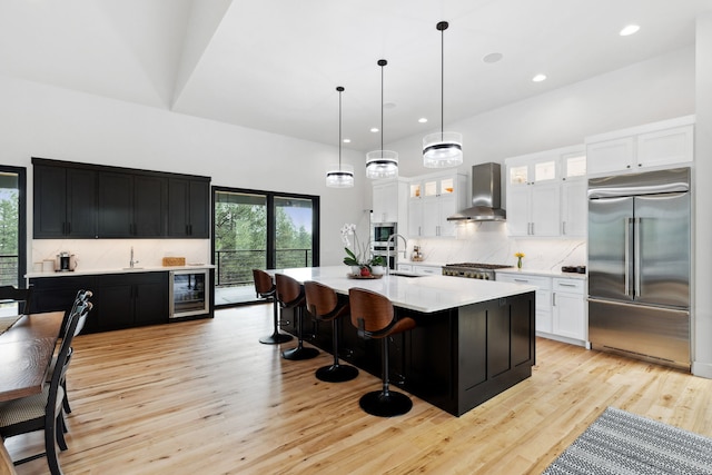 kitchen with beverage cooler, light countertops, wall chimney range hood, dark cabinetry, and built in appliances