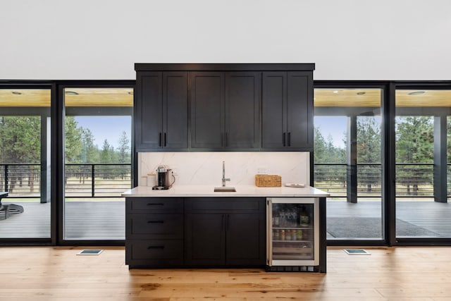 bar with wine cooler, backsplash, and light wood-style flooring