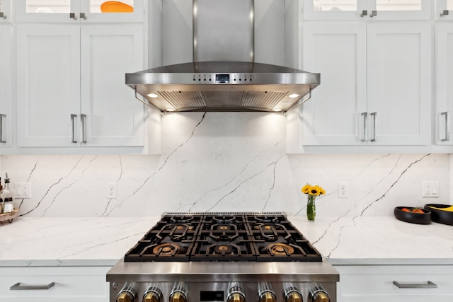 kitchen featuring wall chimney range hood, backsplash, stove, and white cabinets